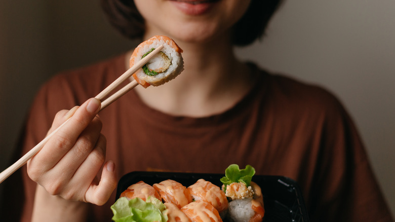 woman holding sushi with chopsticks