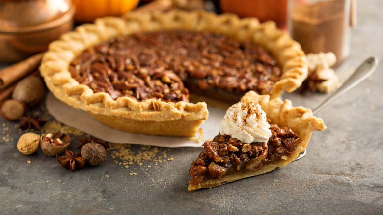 Slice cut from pecan pie topped with whipped cream