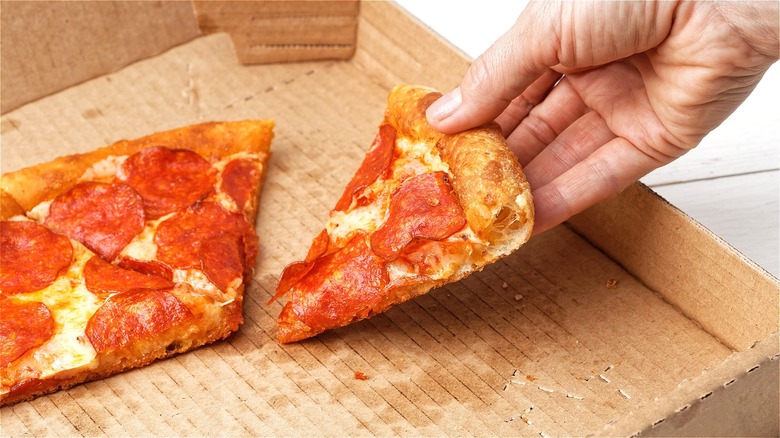 Hand removing pizza slice from box 