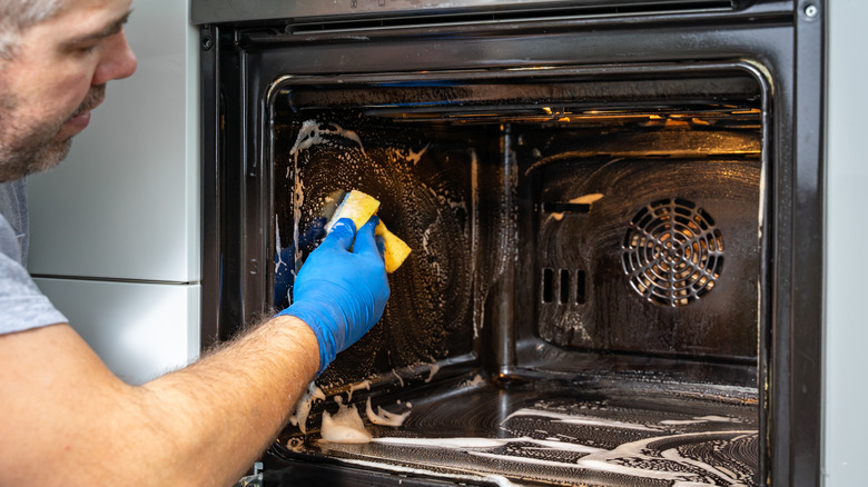 Man cleaning oven with sponge