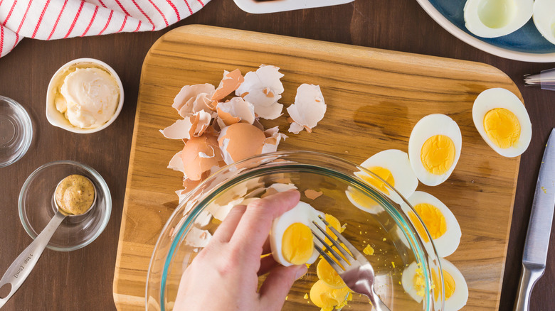 hands removing hard boiled yolks from eggs with fork