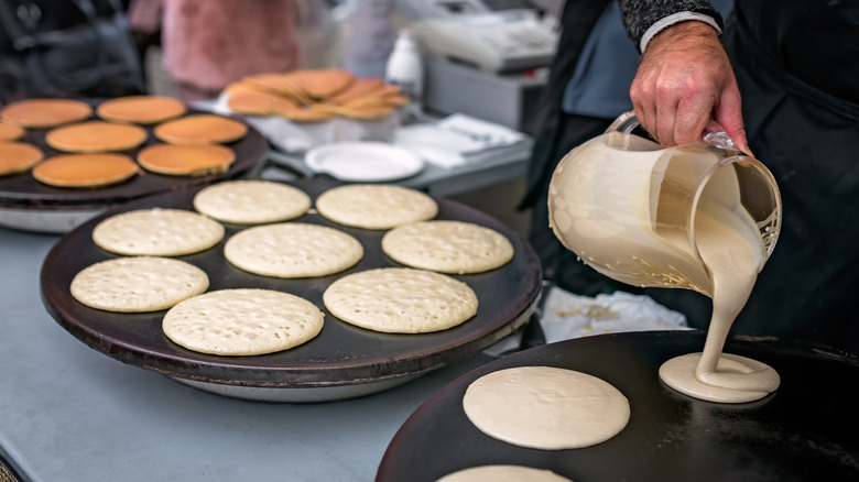 pouring pancakes batter on multiple skillets