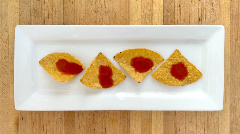 White rectangular plate with tortilla chips topped with Cholula Extra Hot Sauce