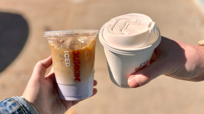 hands holding two Dunkin' coffees