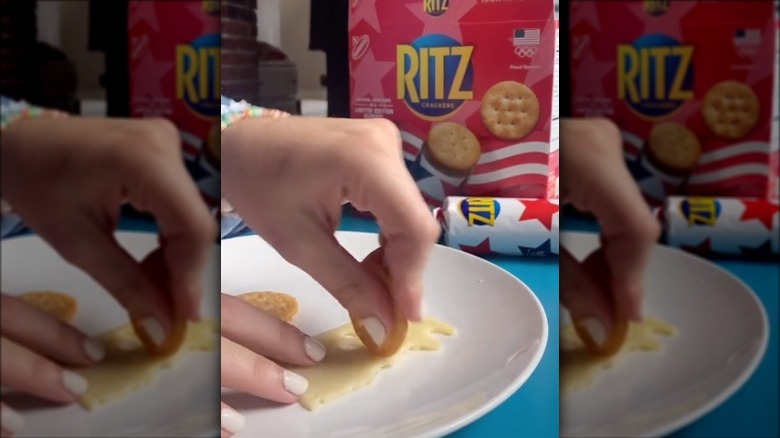 A person cutting cheese with a ritz cracker