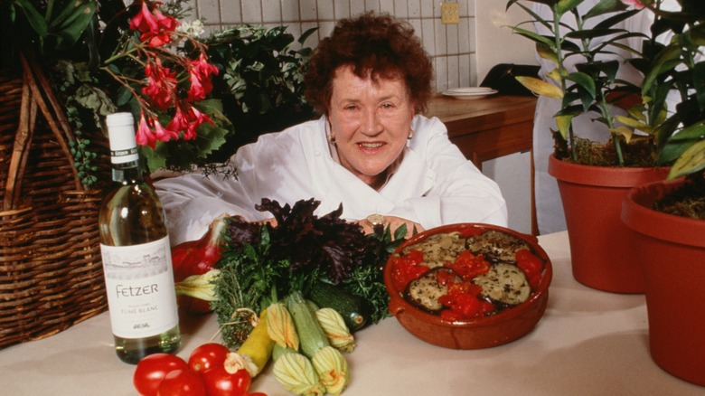 Julia Child posing with vegetables, wine, and Dutch oven