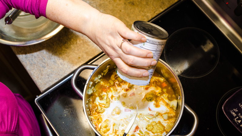 dumping a can of soup into a pot