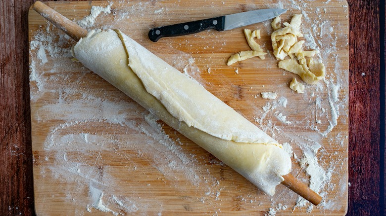 Cutting board with rolling pin wrapped in pastry and scraps to the side