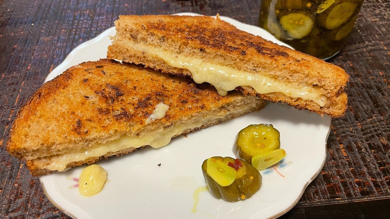 Grilled cheese with cheddar on a white plate with pickles