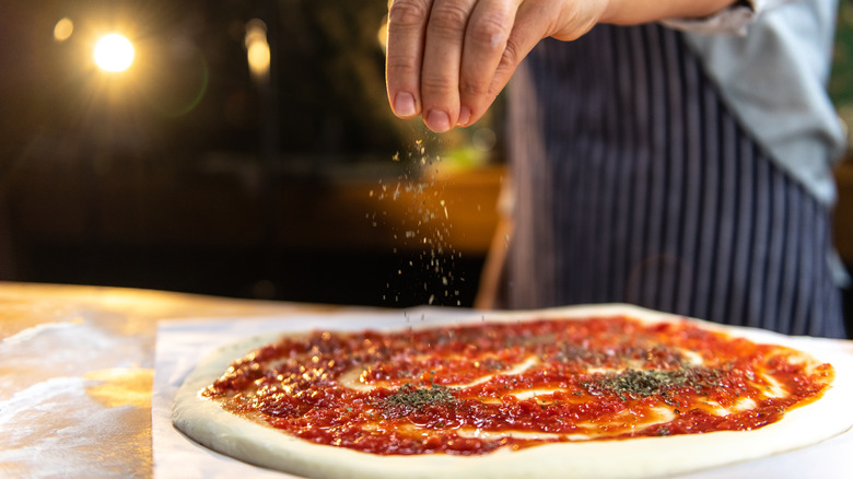 Person adding herbs pizza sauce