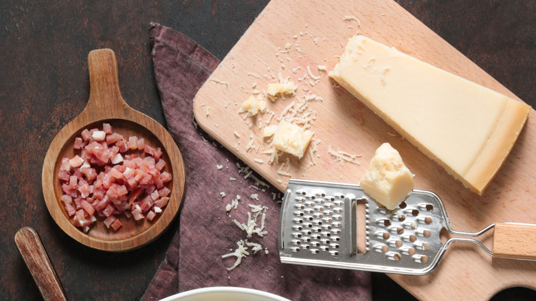 Bacon bits in a wooden dish and a block of parmesan on a cutting board