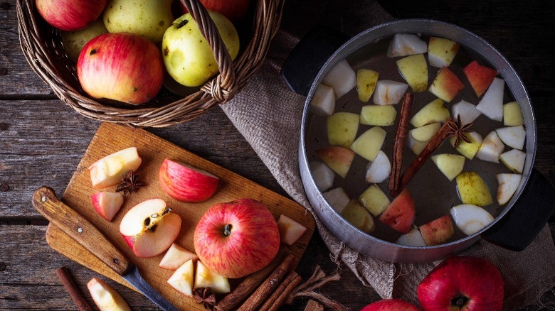 Apples on a cutting board next to a pot of apples and spices in water