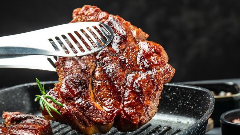 Tongs holding grilled steak