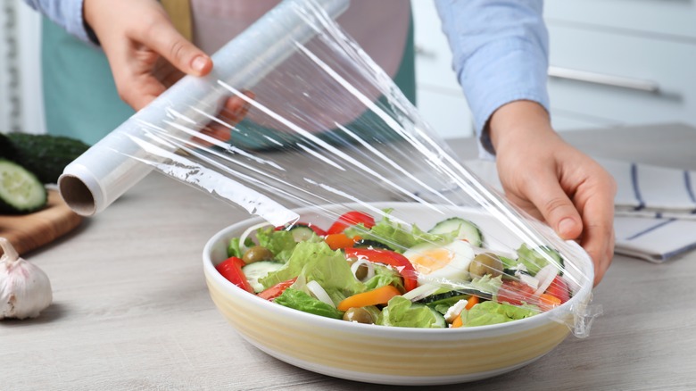 A person wraps a salad in plastic wrap