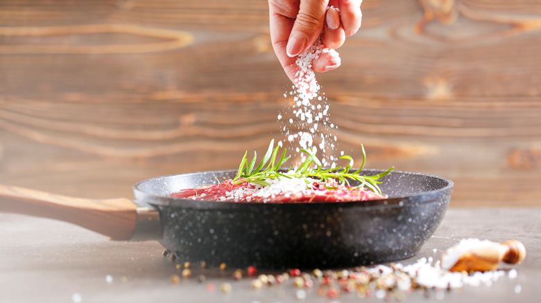 Steak in pan being seasoned