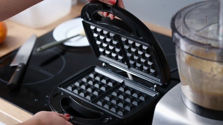 Person opening a waffle iron on a stovetop