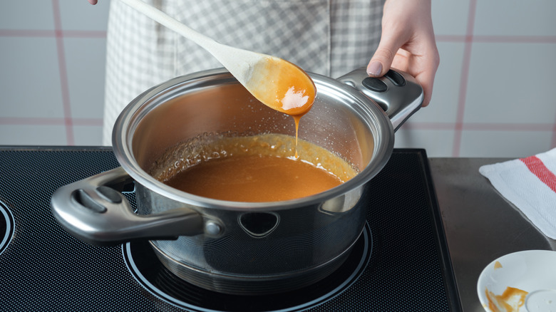 Hands stirring a pot of caramel sauce