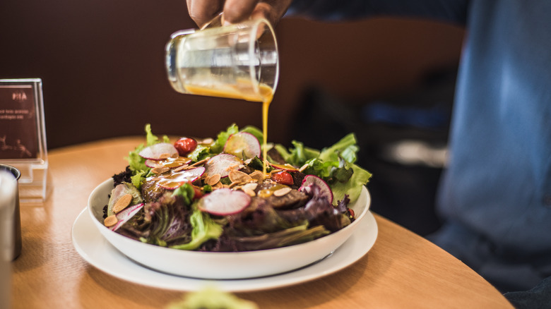 pouring salad dressing on a salad