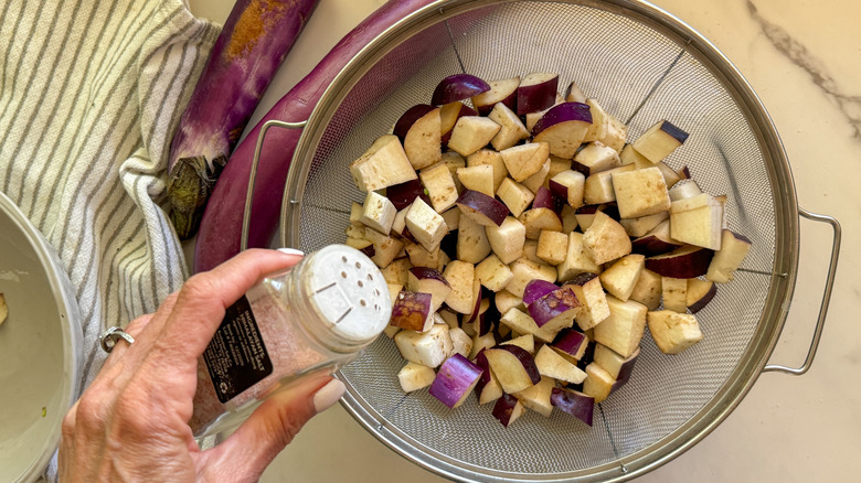 hand salting eggplant in colander