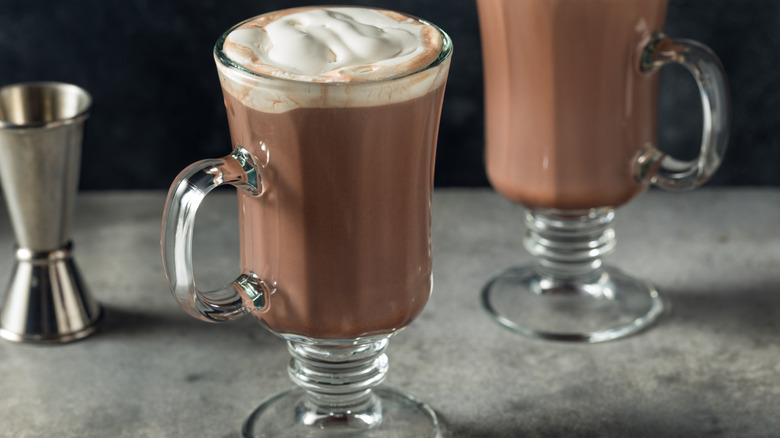 Two boozy hot chocolates with a shot glass in the back.