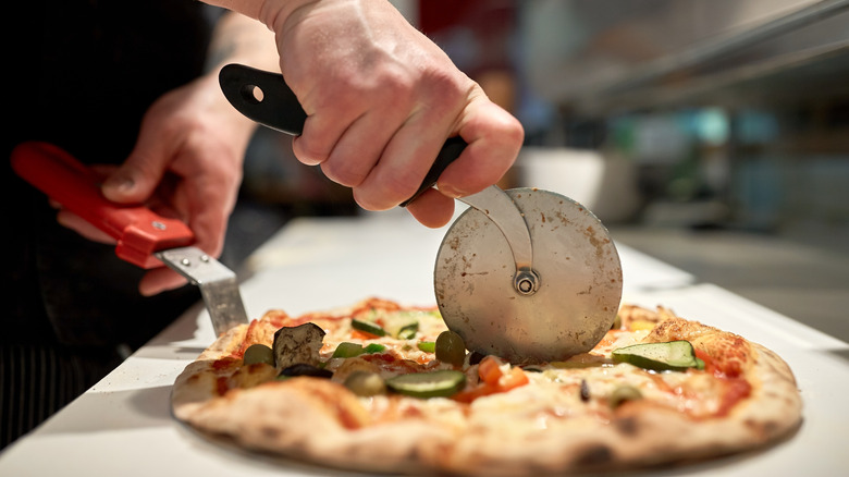 using a pizza cutter to slice a round pizza