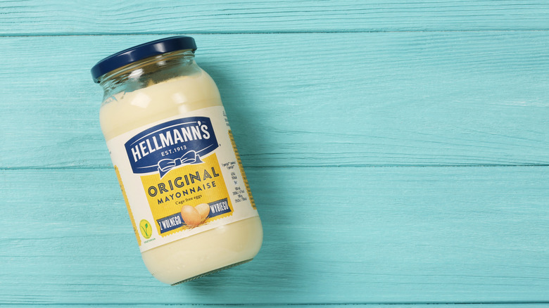 A jar of Hellmann's mayonnaise on a aqua-colored background