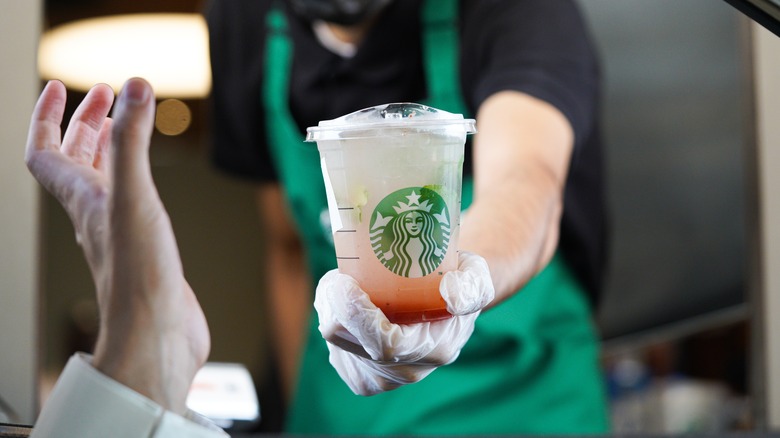 A Starbucks employee hands a customer a drink