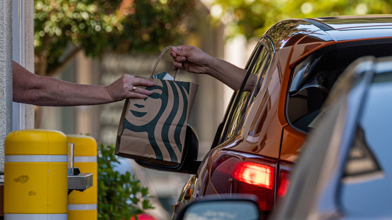 Starbucks worker handing bag through drive-thru window 