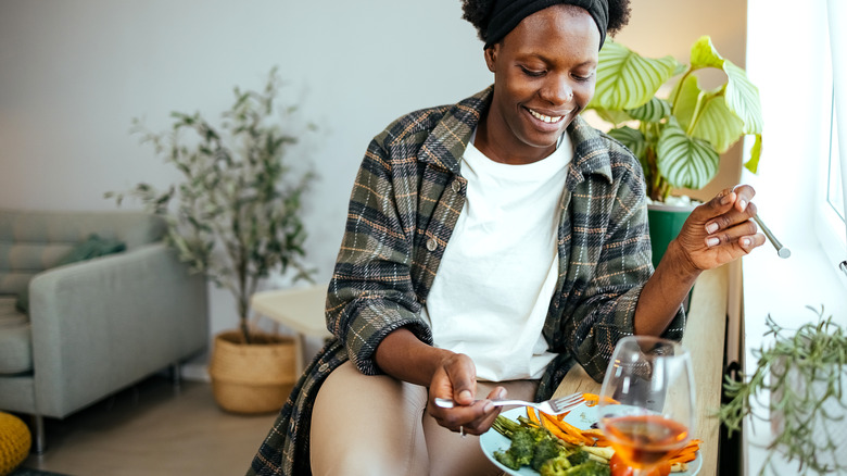 A woman eating veggies with a glass of wine