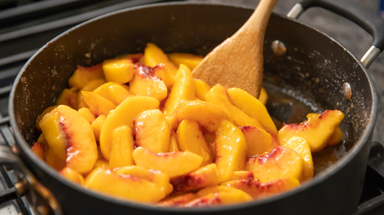 Stewing peaches in a pan with wooden spoon