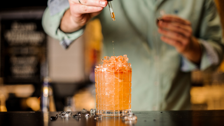 A mixologist drops bitters into a cocktail