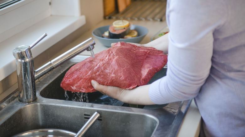 Person rinsing beef in sink