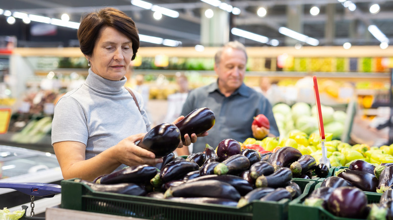 woman chooses eggplant at grocery store