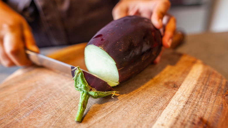 Hands cutting eggplant on wooden cutting board