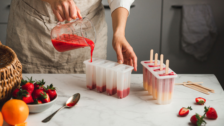 hands pouring juice into popsicle mold on countertop