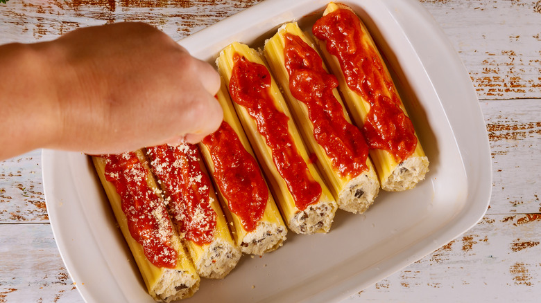 Sprinkling cheese on stuffed manicotti