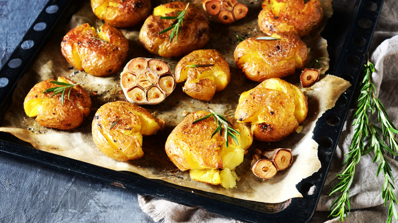 smashed potatoes arranged on baking tray next to rosemary