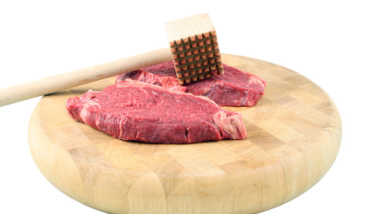 raw steak with meat mallet on wooden board