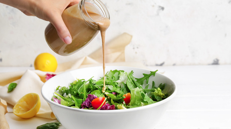 Person pouring tahini over salad