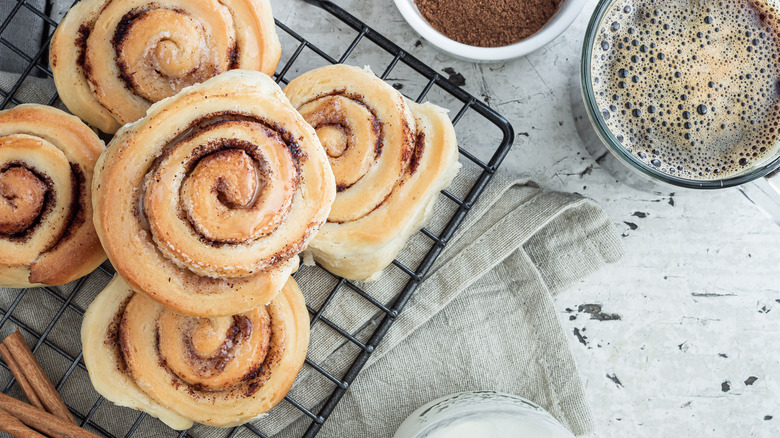 cinnamon rolls on wire baking rack on white table with coffee cup