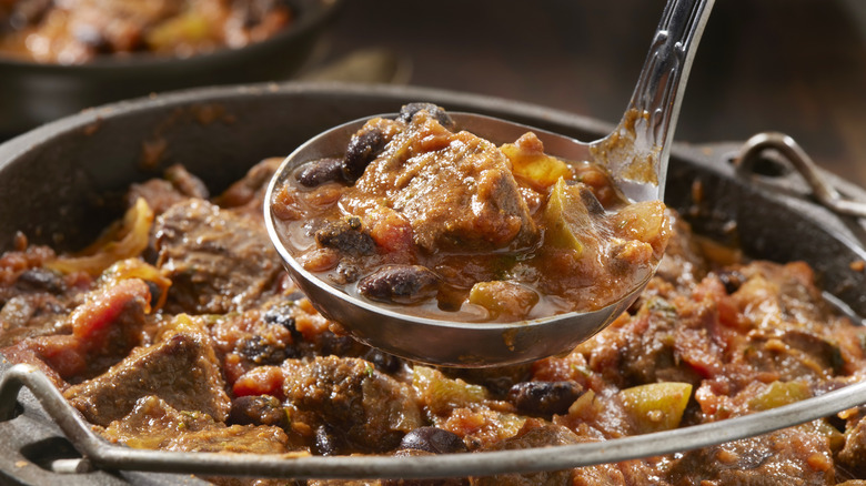 A ladle of steak chili being scooped from a pot