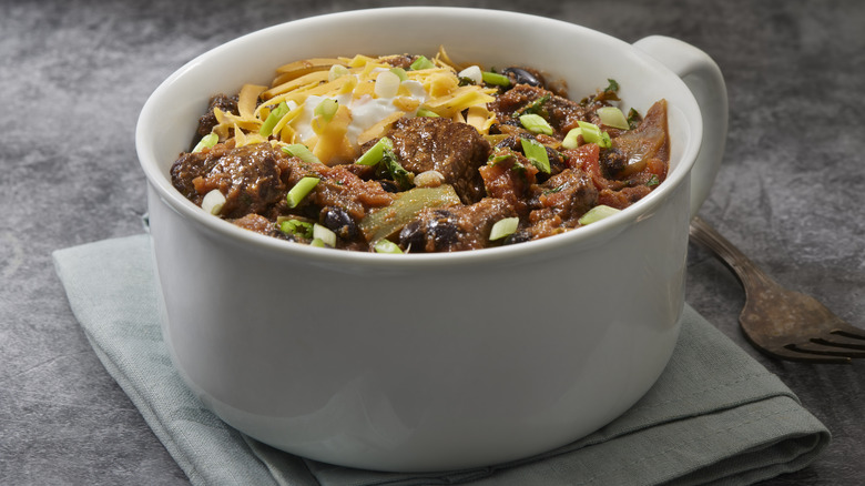 Steak chili in a white bowl with shredded cheese and garnishes