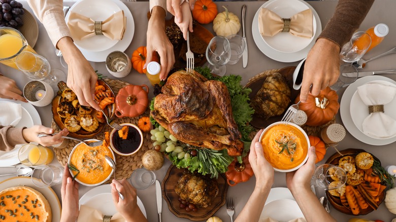 Hands digging into a Thanksgiving meal spread on a table