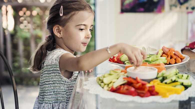 A girl putting a vegetable in dip