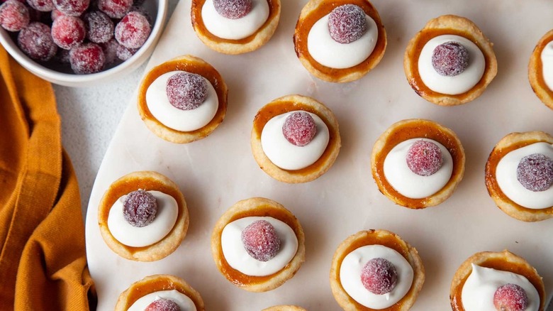 Miniature tarts topped with whipped cream and sugared cranberries