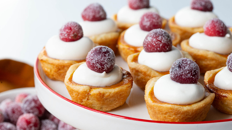 Miniature tarts topped with whipped cream and sugared cranberries