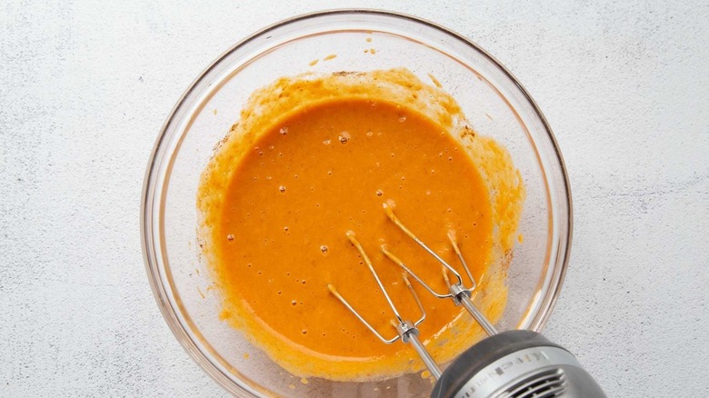 Pumpkin pie filling in a clear bowl with a handheld mixer