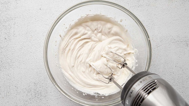 Whipped cream in a clear bowl with a handheld mixer