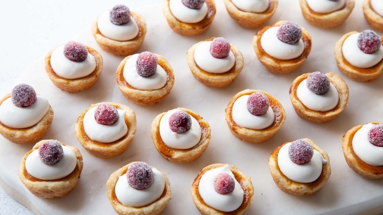 Miniature tarts topped with whipped cream and sugared cranberries