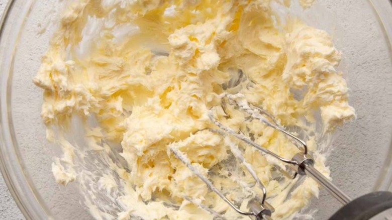 Butter and cream cheese in a clear bowl with a handheld mixer